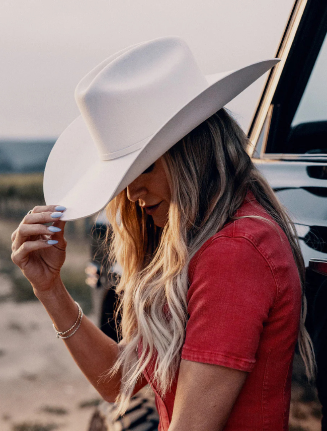 Woman wearing a white cowboy hat and red shirt in front of a vehicle.