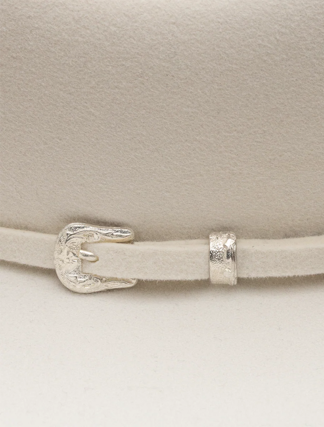 Close-up of a white cowboy hat with a silver buckle and strap on a light background