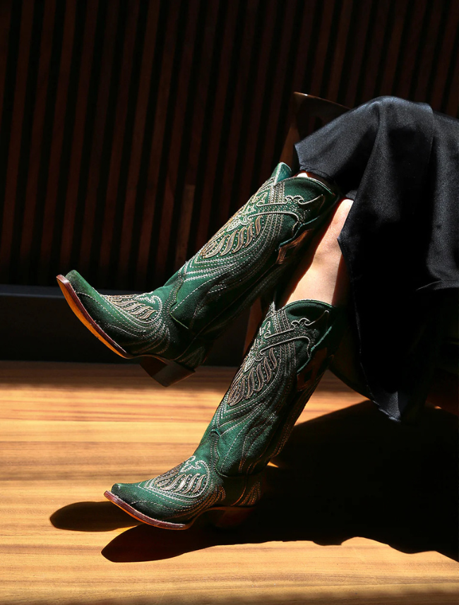 Green embroidered cowboy boots on a wooden floor with a dark background