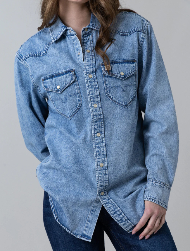 A female model wearing a blue oversized boyfriend button-down denim shirt with two front pockets and pearl snaps.