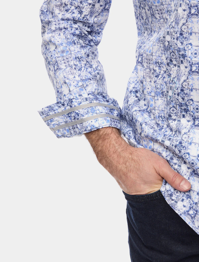 Close-up of a person wearing a blue and white patterned shirt with rolled-up sleeves on a light gray background.