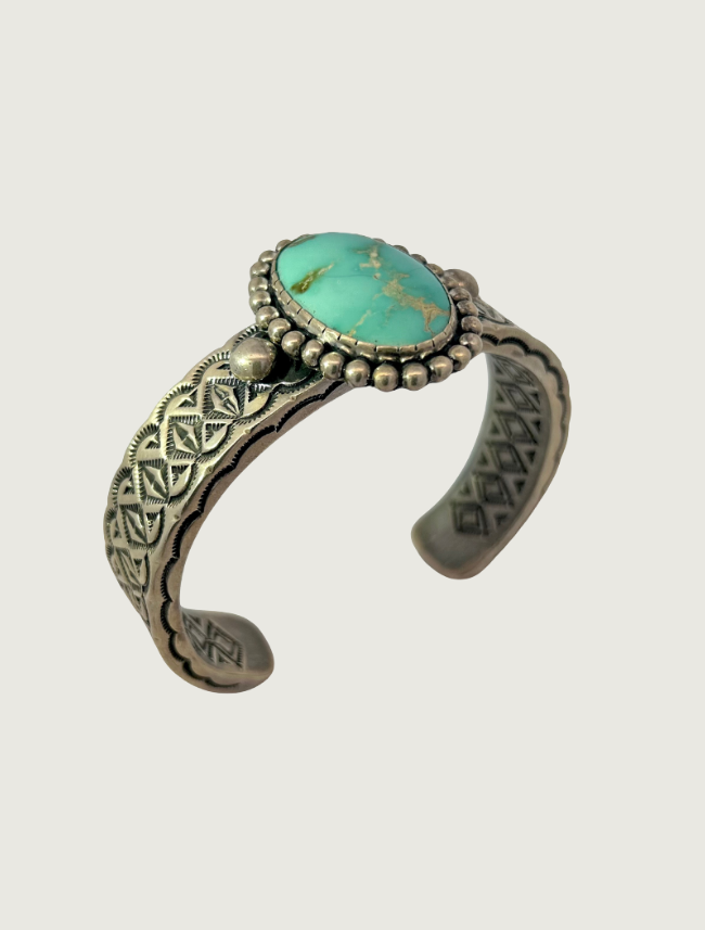 3/4 view of a sterling silver stamped cuff bracelet by Johnathan Nez with a turquoise stone in a beaded bezel setting