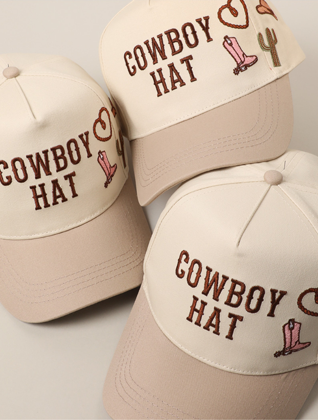 Front view of a beige trucker hat with embroidered designs including “COWBOY HAT,” a pink boot, rope heart, and cactus.
