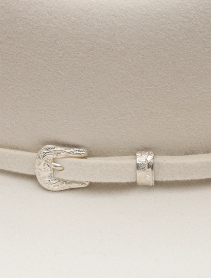 Close-up of a white cowboy hat with a silver buckle and strap on a light background