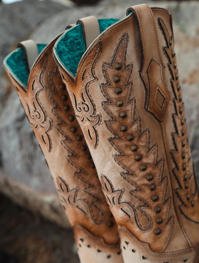 Pair of tan cowboy boots with intricate designs on a textured surface