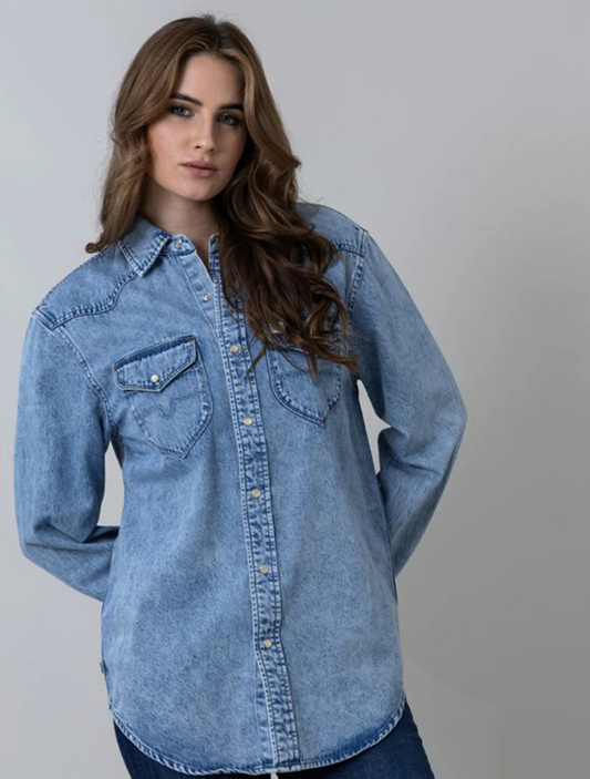 A female model wearing a blue oversized boyfriend button-down denim shirt with two front pockets and pearl snaps.