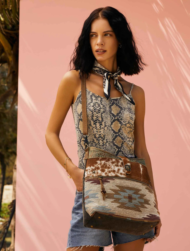 Woman wearing a patterned dress and carrying a crossbody bag with a pink background