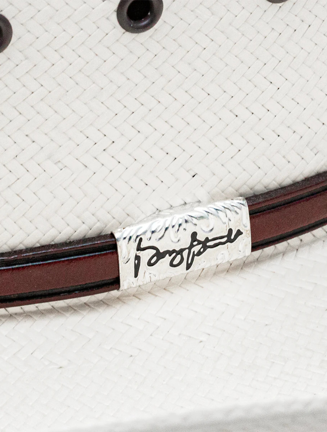 Close-up of a white straw cowboy hat with a brown band and a label featuring a signature.