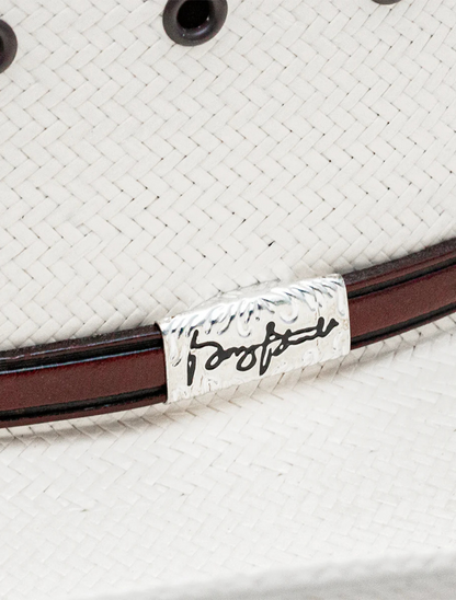 Close-up of a white straw cowboy hat with a brown band and a label featuring a signature.