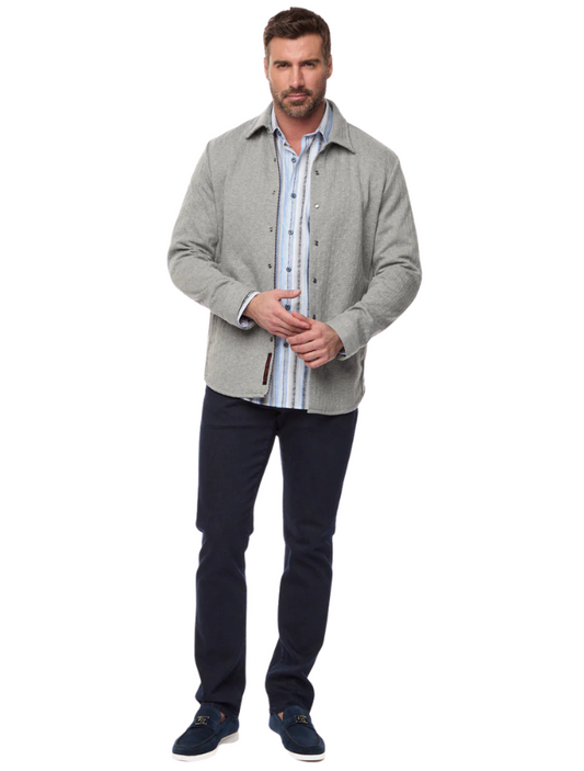 Man wearing a grey, knit jacket on a white background. He is also wearing a patterned button up shirt and dark jeans.