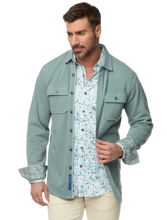 Man wearing a light blue textured shirt over a patterned shirt on a white background