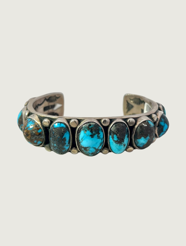 Orville Tsinnie sterling silver row cuff bracelet featuring oval Bisbee Blue turquoise cabochons with dark matrix in bezel settings, with silver bead accents and stampwork on the inner band